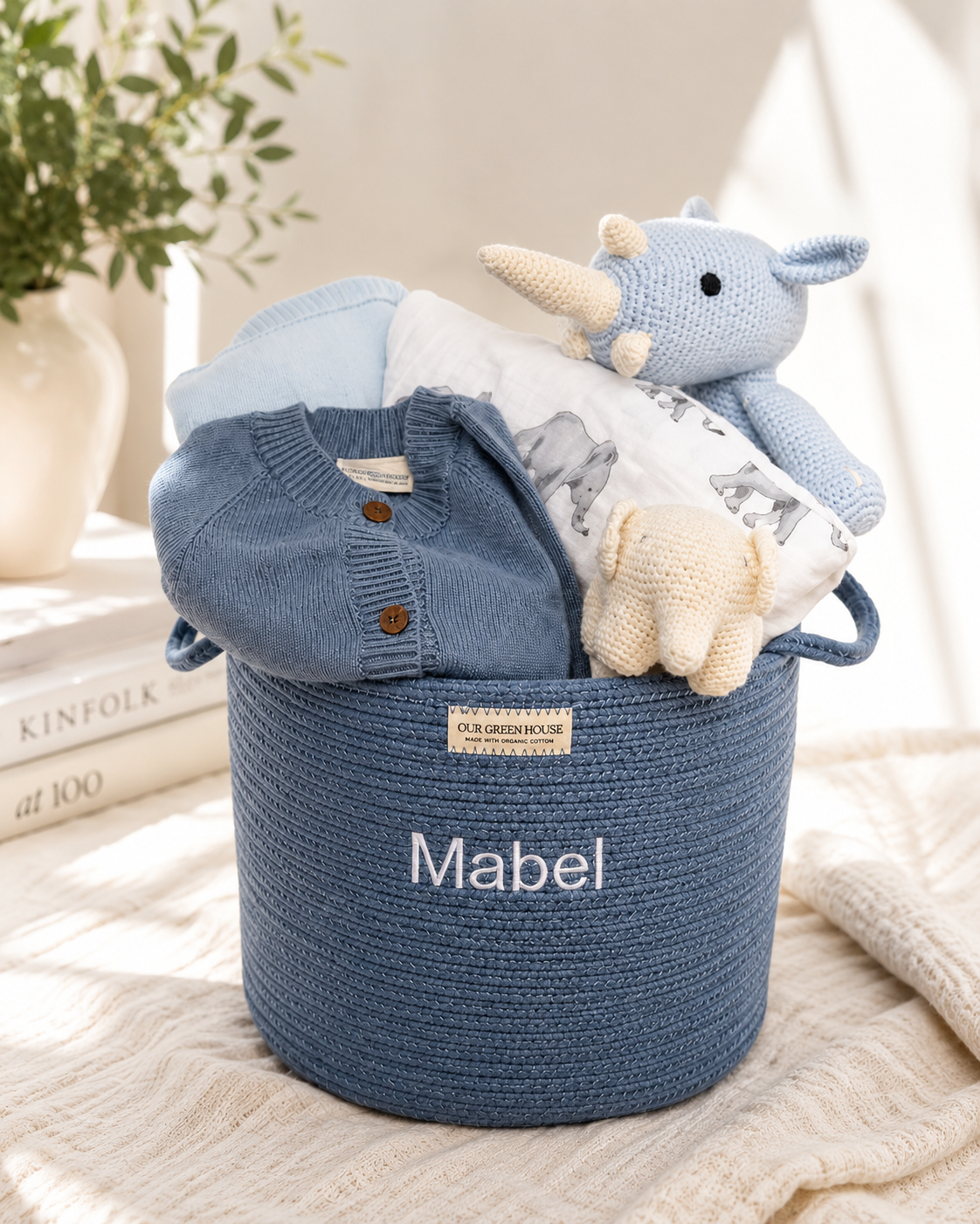 Blue Our Green House baby gift basket with a personalized woven basket, knit rhino toy, baby cardigan, soft blanket, and newborn essentials.