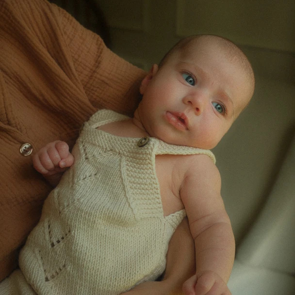 Baby wearing a knitted outfit and looking up.