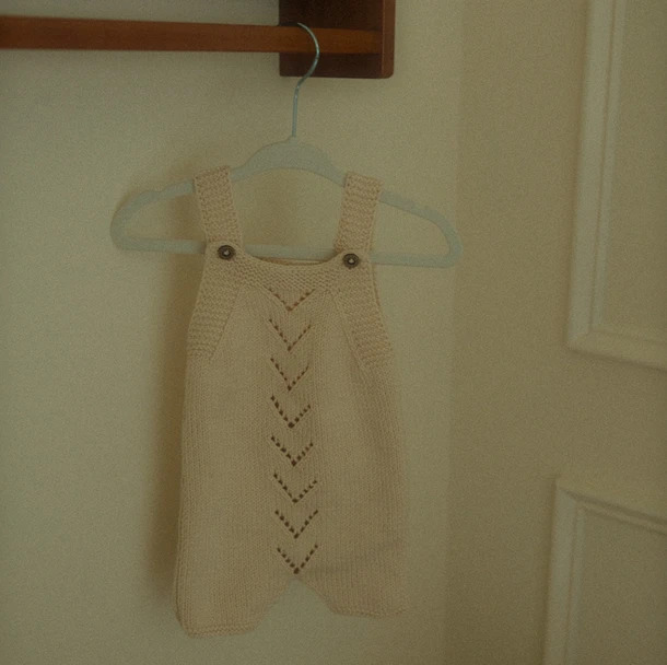 Knitted baby outfit hanging on a clothes hanger.