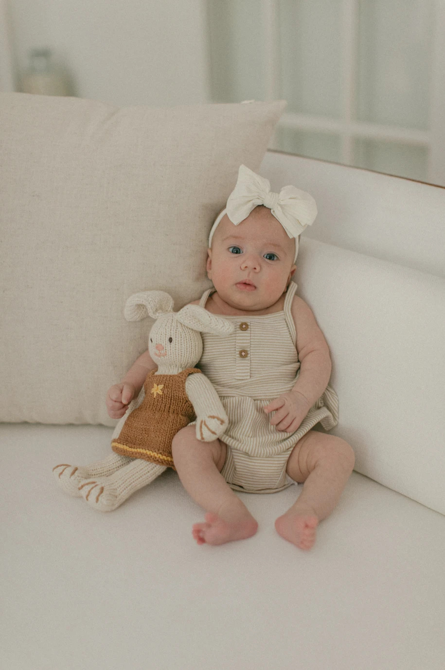 Baby sitting with a knitted bunny toy.