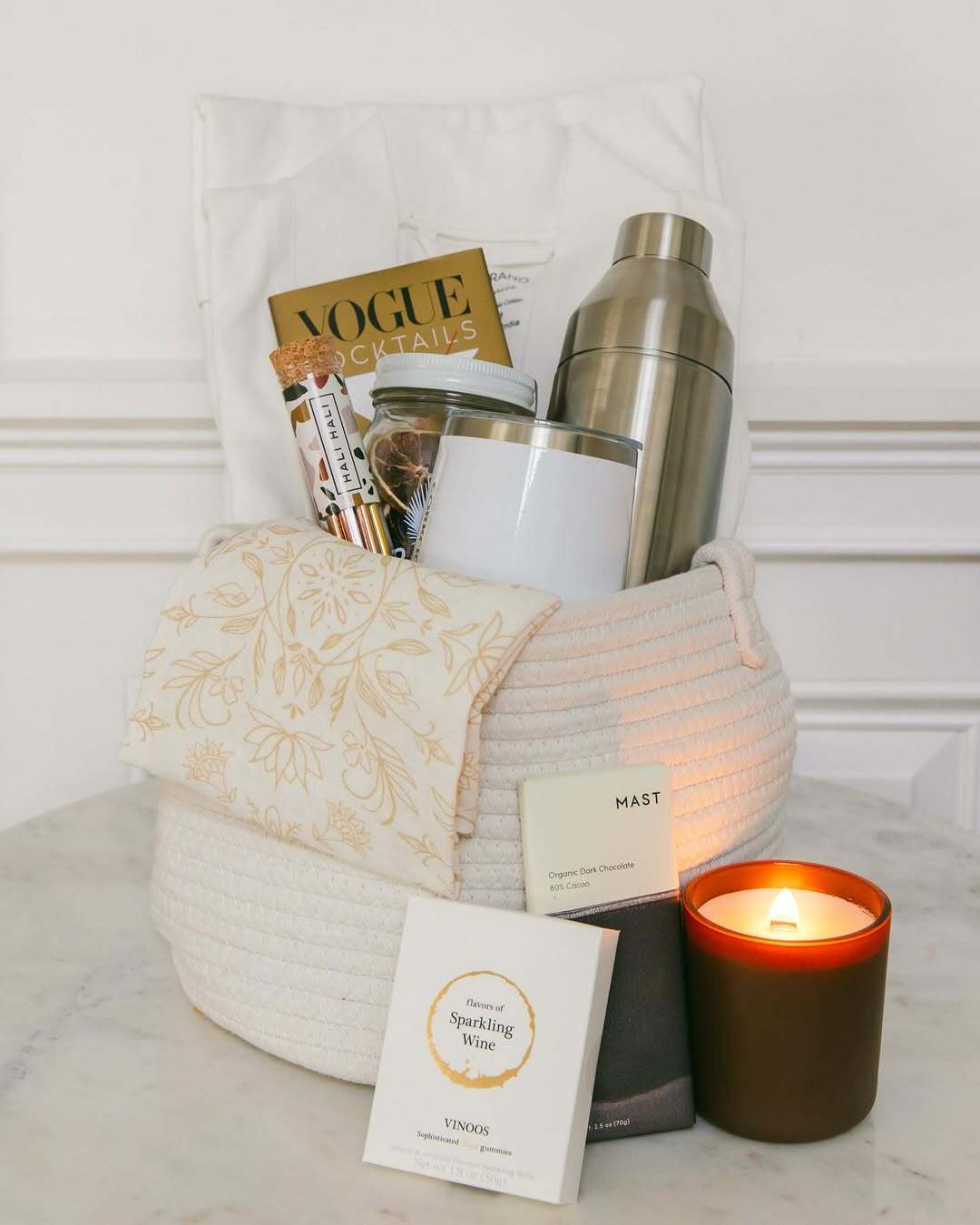Our Green House gift basket with a cocktail shaker, Vogue book, chocolate, wine gummies, and a glowing candle.