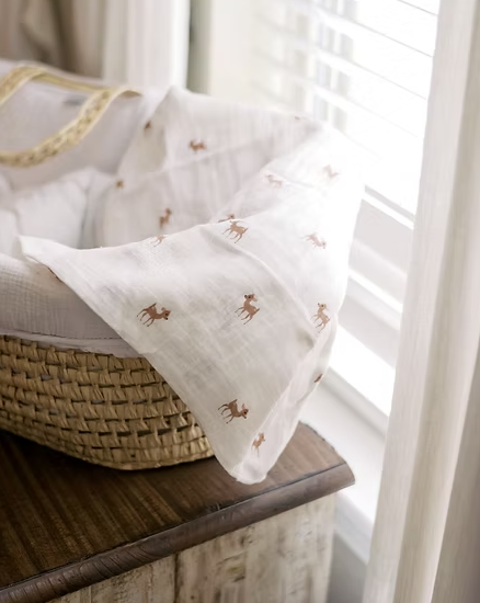 White muslin swaddle with brown deer print draped over a woven basket in natural light from Our Green House.