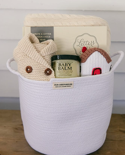 White cotton rope basket from Our Green House filled with baby balm, knit sweater, toy, and a keepsake book