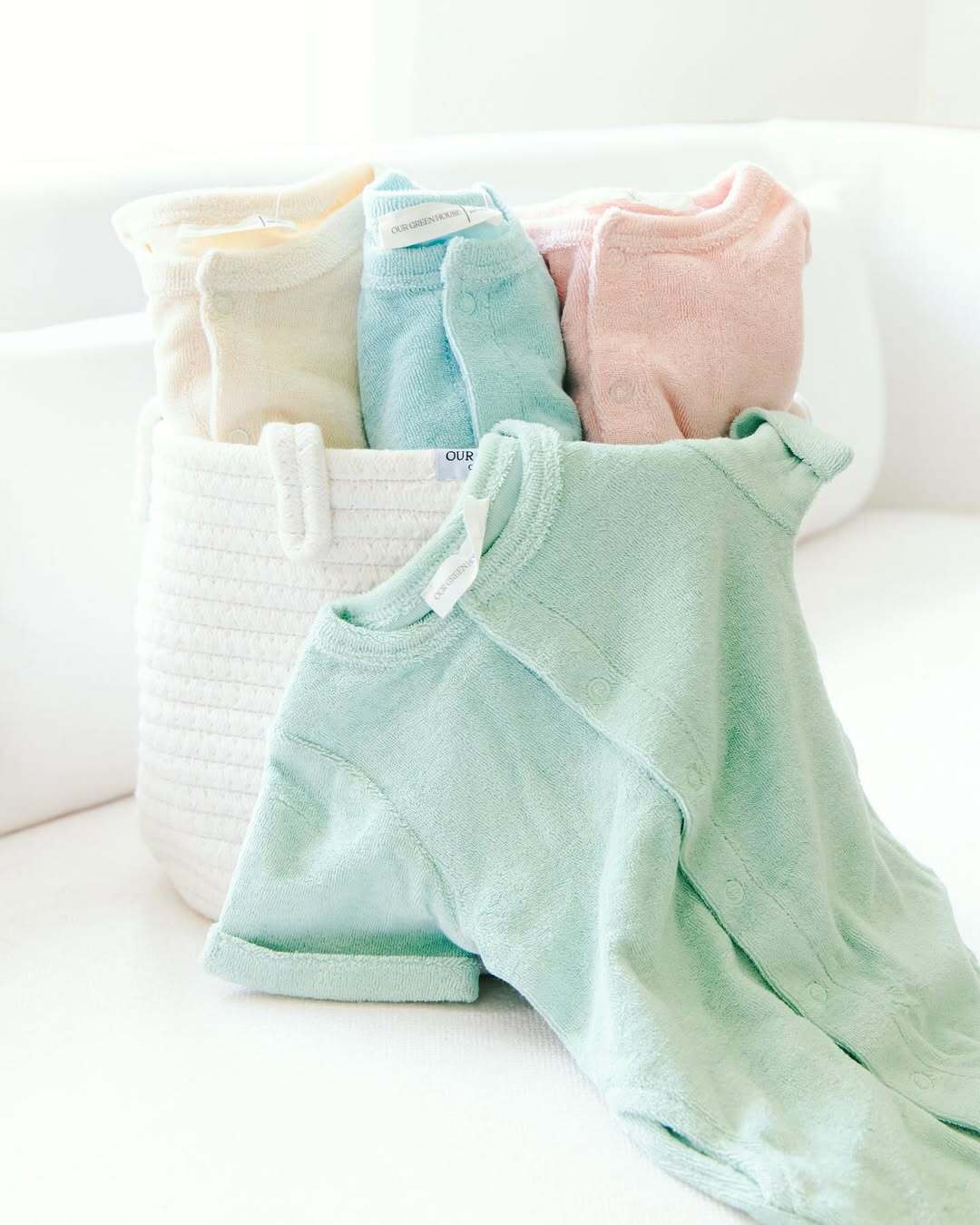 Mint green baby romper draped over a white woven basket filled with baby clothes from Our Green House.