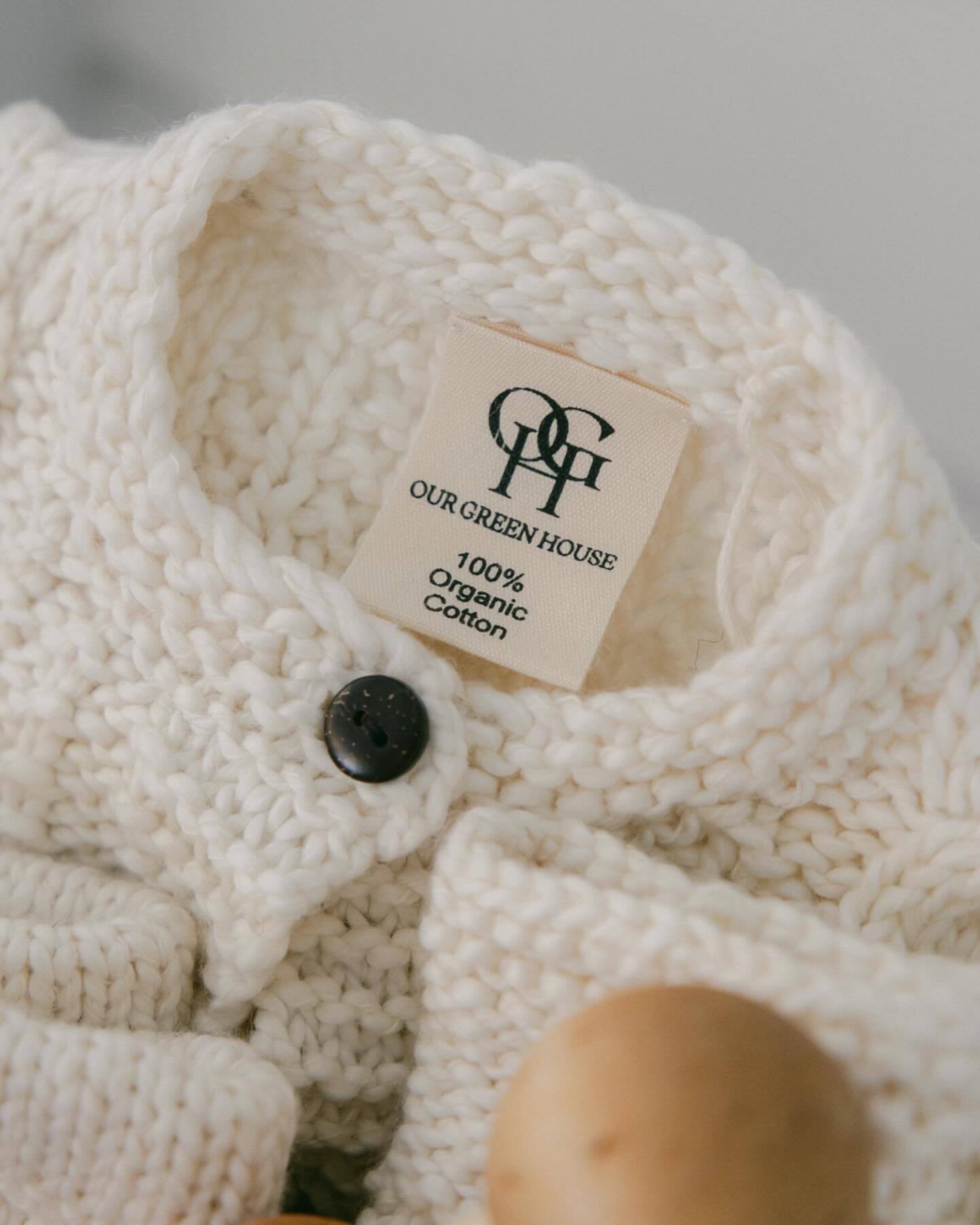 A 100% organic cotton tag shown on a handknit organic baby sweater by Our Green House.