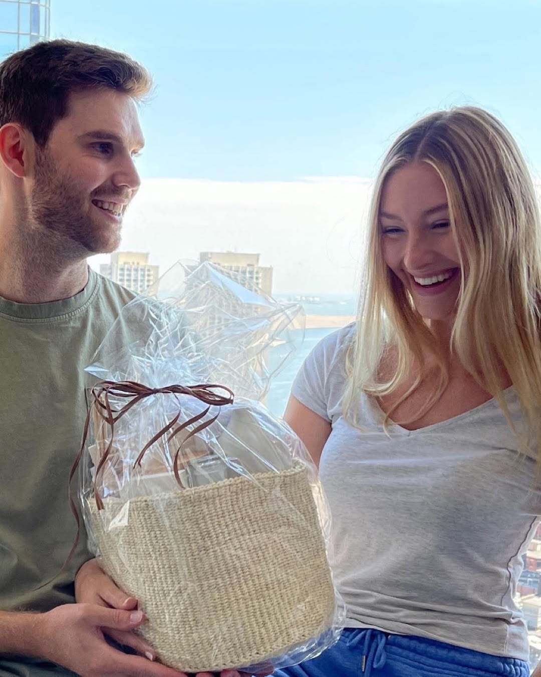 A couple holding an Our Green House gift basket outdoors with a city skyline in the background.