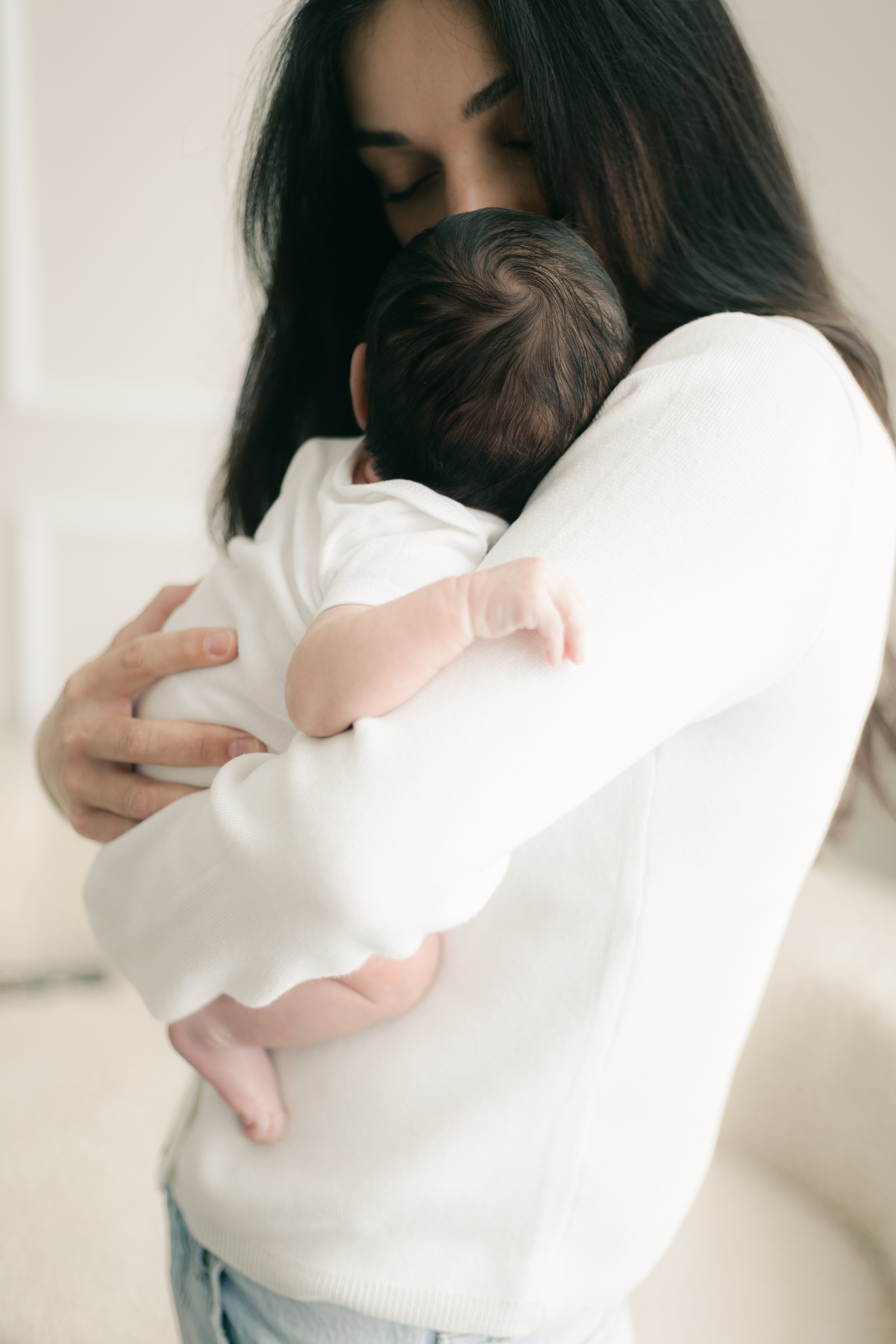 Mother gently holding her newborn wrapped in a soft white outfit during a quiet moment at home.