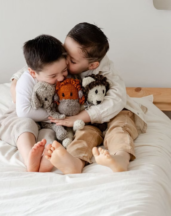 Two kids hugging stuffed animals in bed.