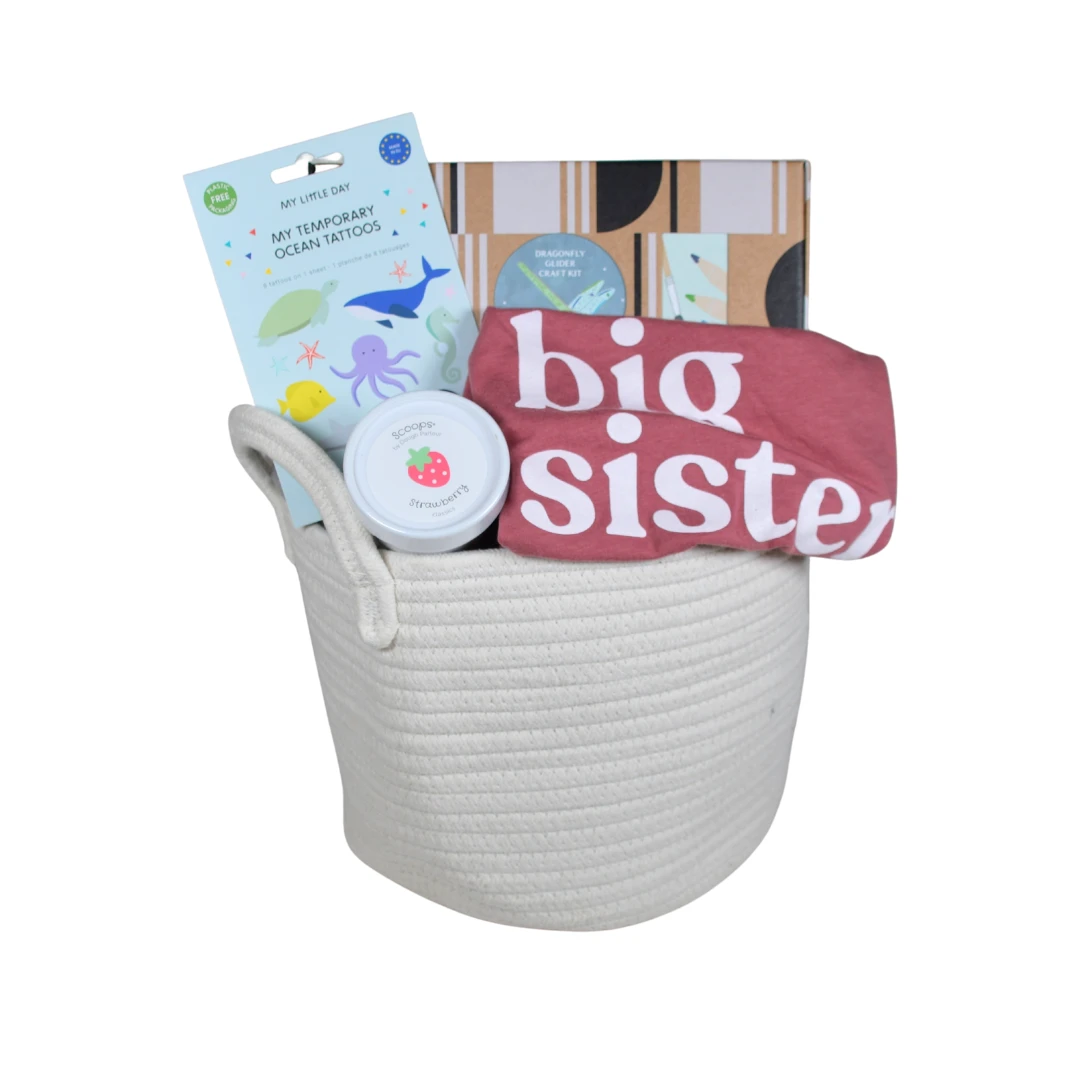 Our Green House big sister gift basket with a pink shirt, activity book, keepsake tin, and striped storage box for new siblings.