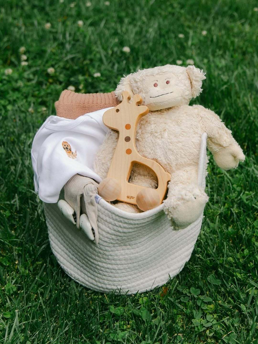 A baby gift basket with a plush toy, a wooden giraffe rattle, and a onesie by Our Green House.