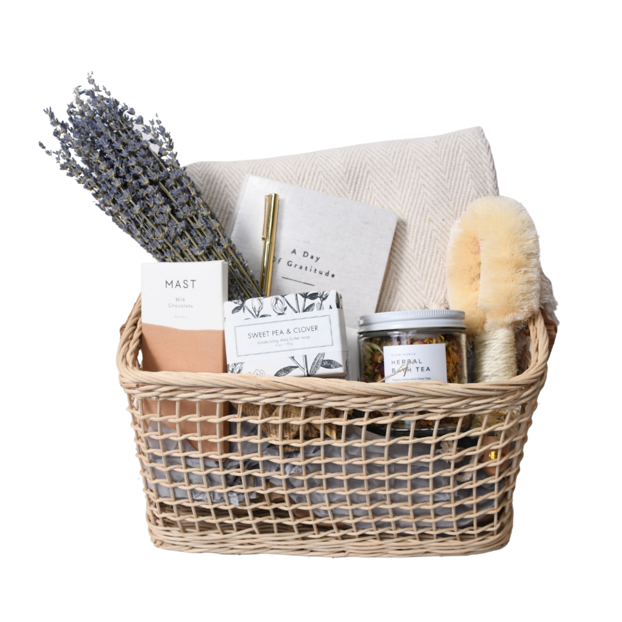 Our Green House wellness basket with lavender, chocolate, journal, soap, herbal tea, brush, and blanket.