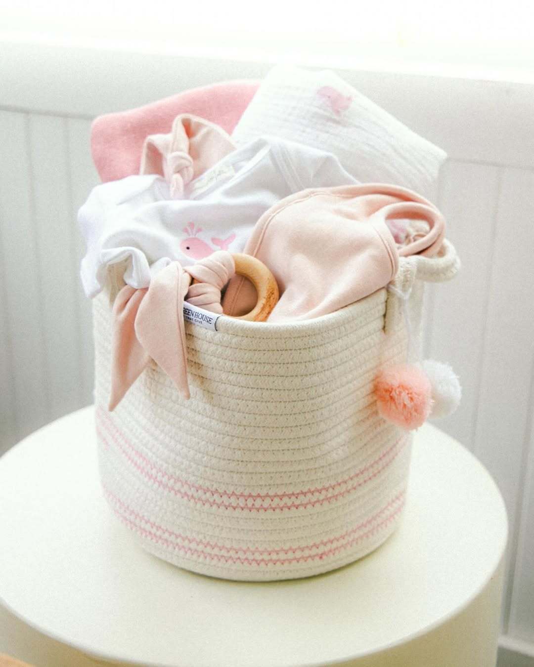White and pink woven basket brimming with GOTS‑certified organic baby garments, emphasizing softness and safety.