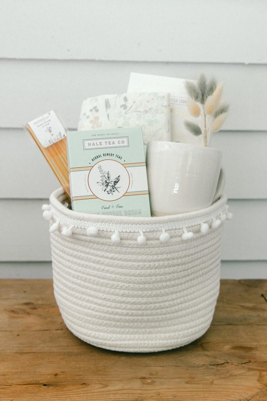 Our Green House white rope spa gift basket with herbal tea, ceramic mug, natural soap, and dried floral accents.