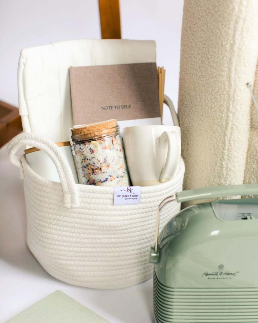 Our Green House gift basket with bath salts, mug, and journal in a white woven bin, perfect for cozy self-care.
