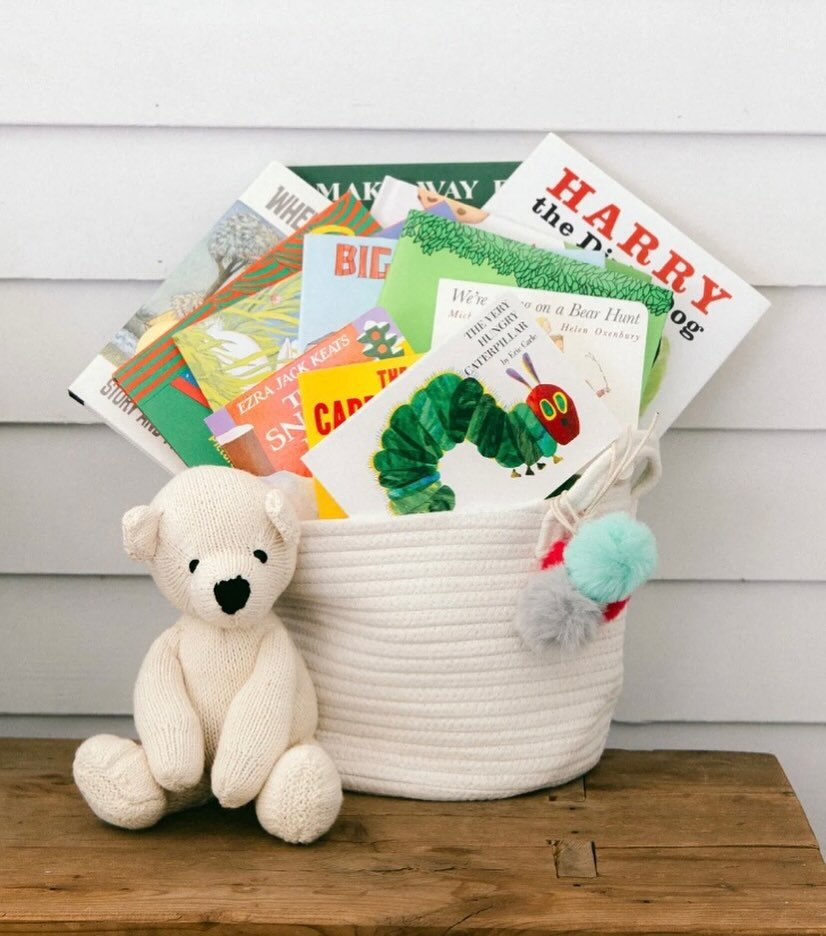 White woven basket from Our Green House filled with colorful books and a teddy.